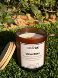 An amber glass candle with a label that says "Velvet Hour" along with a short blurb reading "A touch of bergamot meets steeped black tea, creating an after-dark scent designed for comfort and sophistication."