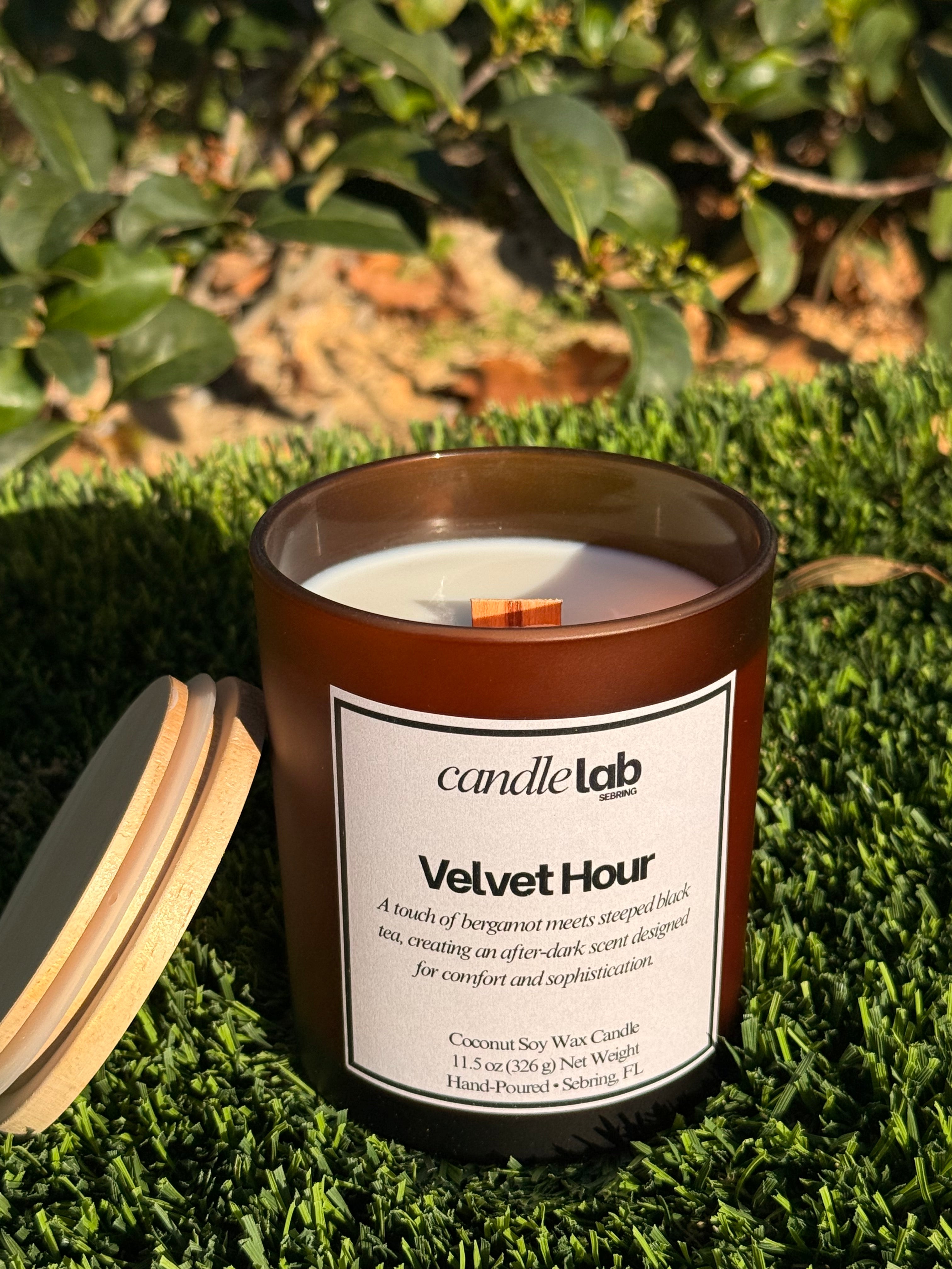 An amber glass candle with a label that says "Velvet Hour" along with a short blurb reading "A touch of bergamot meets steeped black tea, creating an after-dark scent designed for comfort and sophistication."