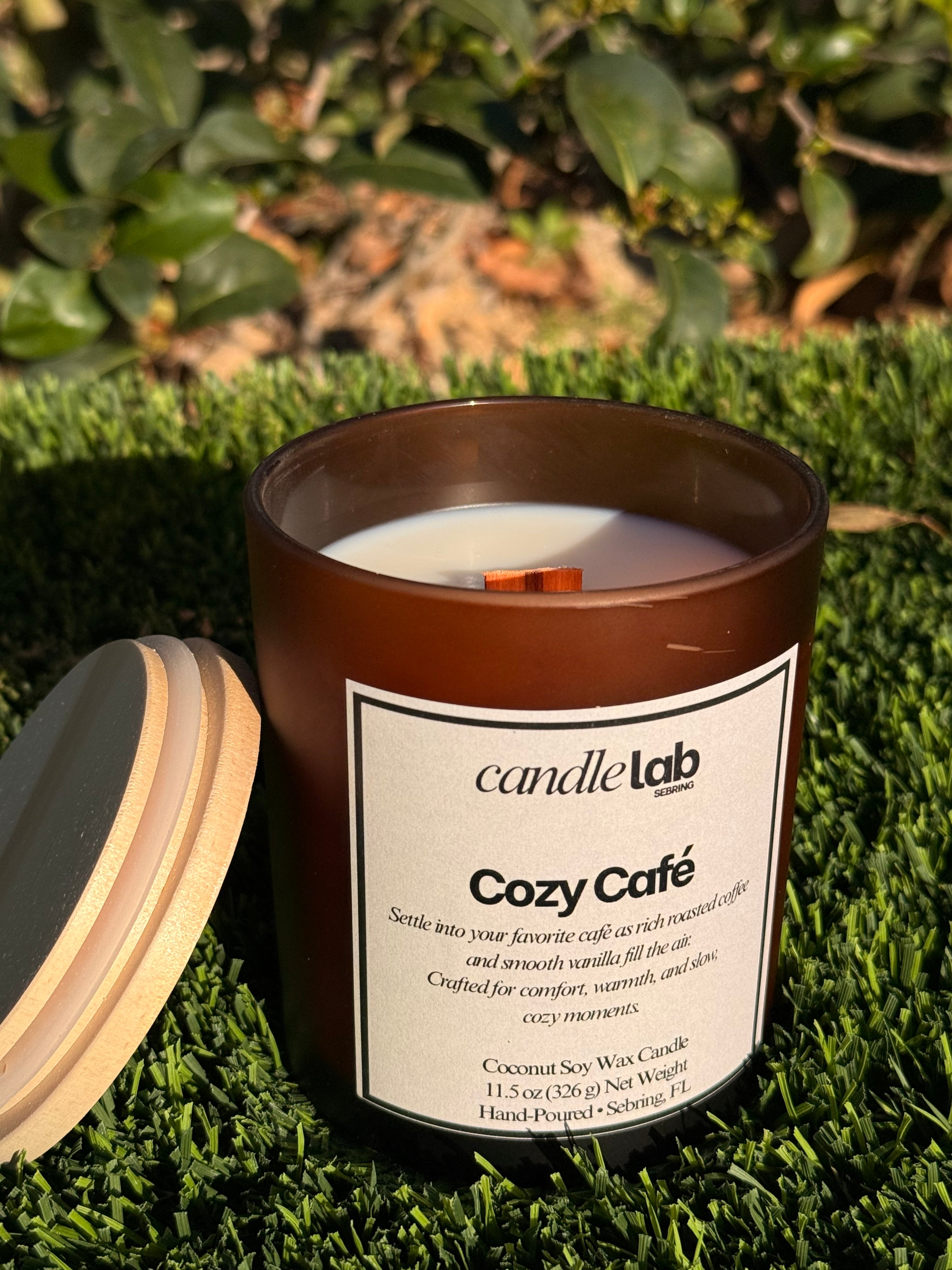 An amber glass candle with a label that says "Cozy Cafe" along a short blurb reading "Settle into your favorite cafe as rich roasted coffee and smooth vanilla fill the air. Crafted for comfort, warmth, and silent, cozy moments."