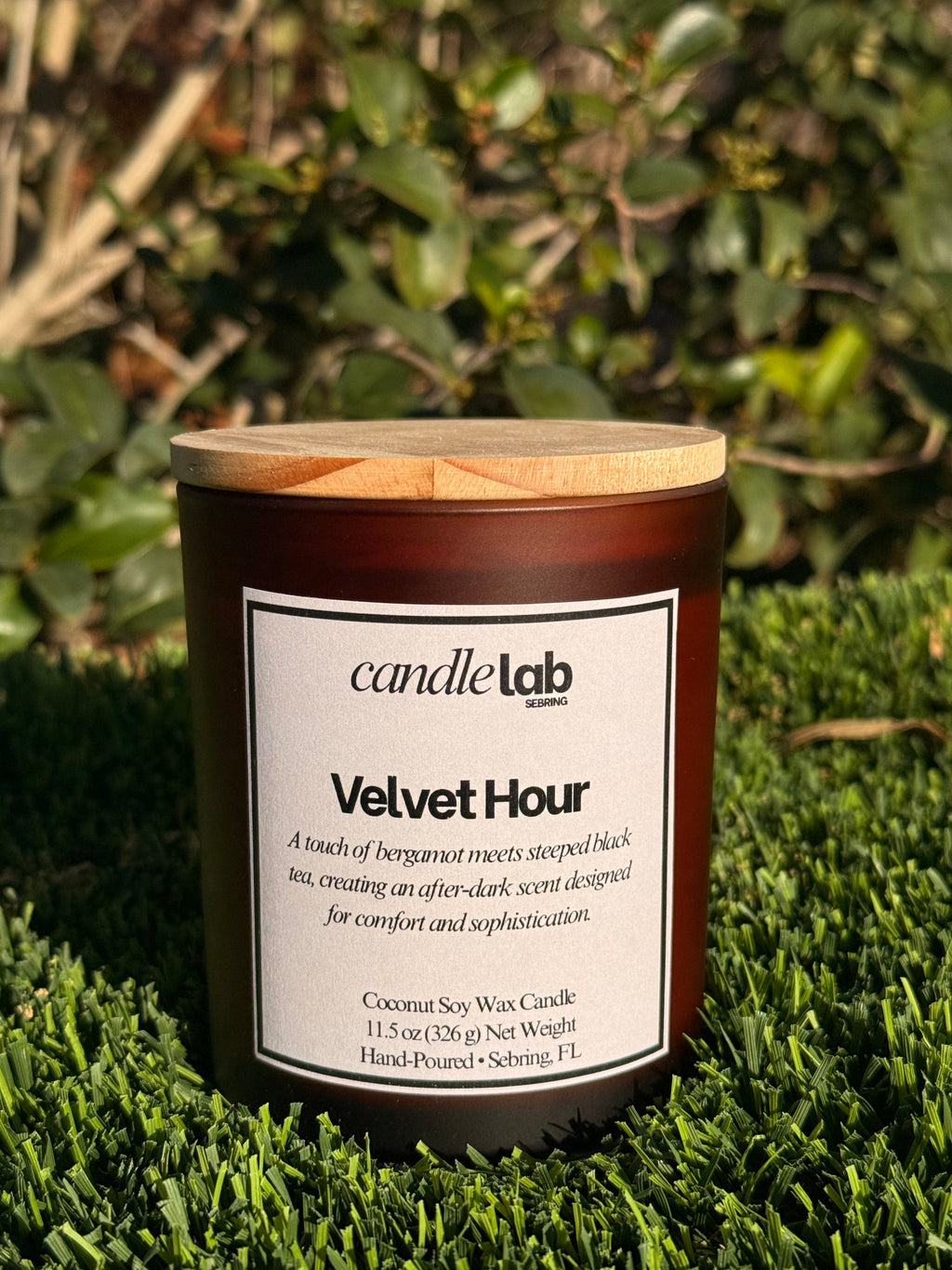 An amber glass candle with a label that says "Velvet Hour" along with a short blurb reading "A touch of bergamot meets steeped black tea, creating an after-dark scent designed for comfort and sophistication."