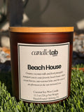 An amber glass candle with a label that says "Beach House" along with a short blurb reading "Creamy coconut milk and fresh pineapple transport you to your favorite beach house, where ocean breezes, sun-warmed skin, and the ease of an afternoon in the Sun surround you."