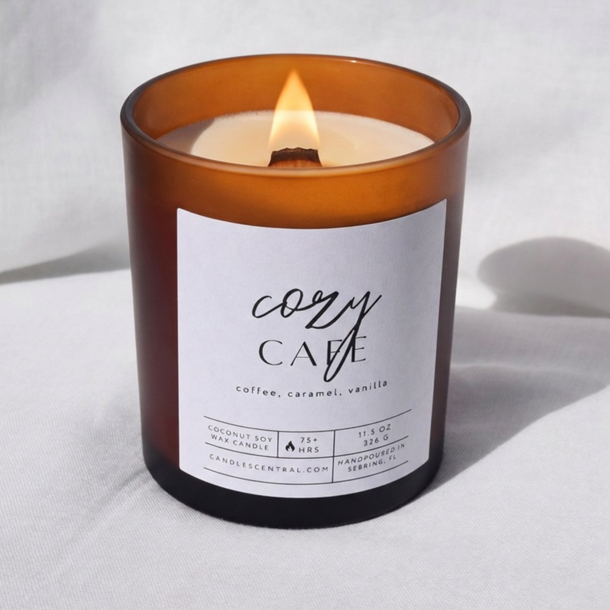 Picture of a candle burning with a label that says "Cozy Cafe" along with the fragrance notes of coffee, caramel, and vanilla