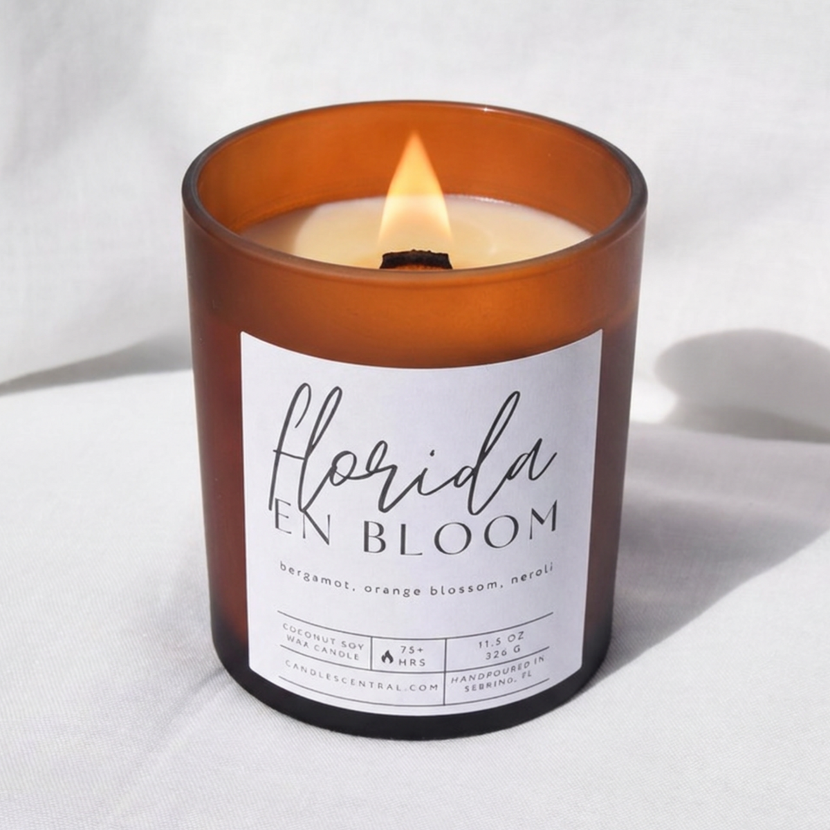 Picture of a candle burning with a label that says "Florida en Bloom" along with the fragrance notes of bergamot, orange blossom, and neroli