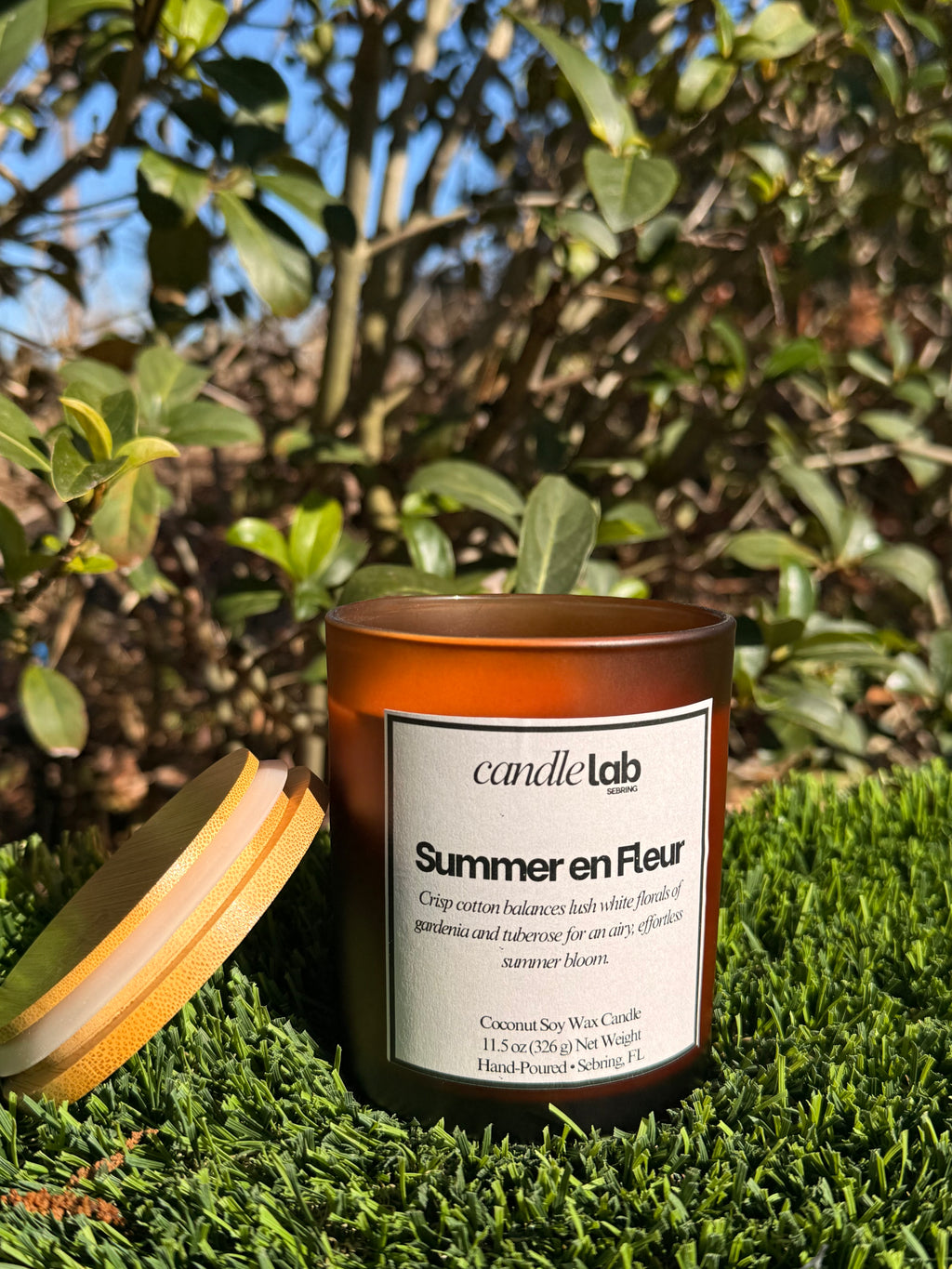 An amber glass candle with a label that says "Summer en Fleur" along with a short blurb that reads "Crisp cotton balances lush white florals of gardenia and tuberose for an airy, effortless summer bloom."