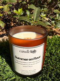 An amber glass candle with a label that says "Summer en Fleur" along with a short blurb that reads "Crisp cotton balances lush white florals of gardenia and tuberose for an airy, effortless summer bloom."