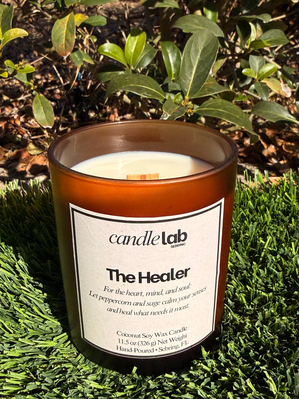 An amber glass candle with a label that says "The Healer" along with a short blurb that reads "For the heart, mind, and soul: Let peppercorn and sage calm your senses and heal what needs it most."
