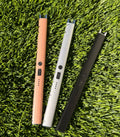 A picture of three electric lighters laying on a grass background. One is bronze, one is silver, and one is black.