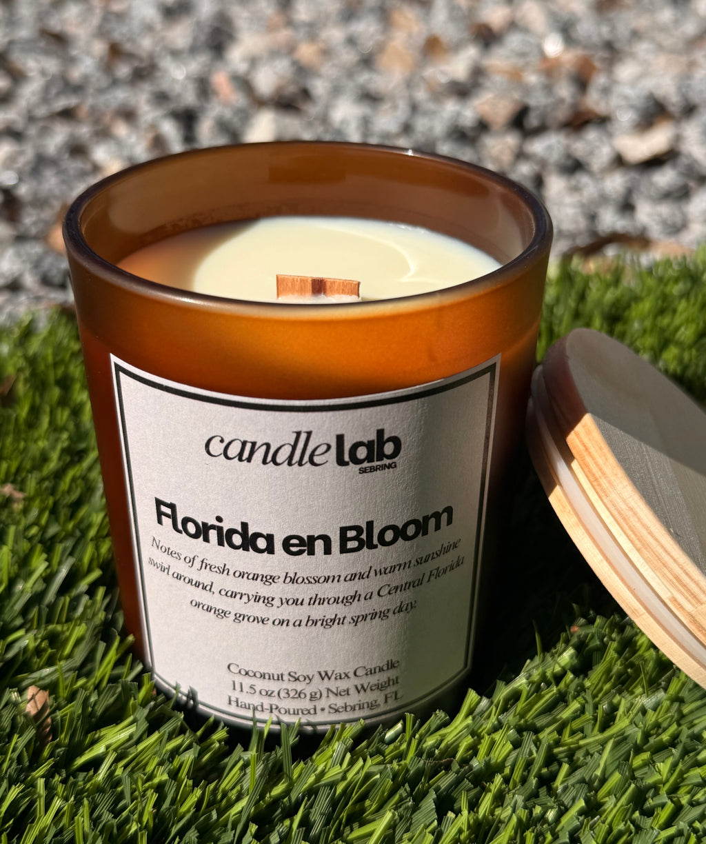 An amber glass candle with a label that says "Florida en Bloom" along with a short blurb that reads "Notes of fresh orange blossom and warm sunshine swirl around, carrying you through a Central Florida orange grove on a bright spring day."