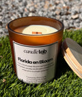 An amber glass candle with a label that says "Florida en Bloom" along with a short blurb that reads "Notes of fresh orange blossom and warm sunshine swirl around, carrying you through a Central Florida orange grove on a bright spring day."