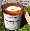 An amber glass candle with a label that says "Strawberry Fields" along with a short blurb reading "Wander through rows of sun-ripened strawberries, where the air is filled with the scent of simple summer sweetness."