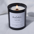 Picture of a candle burning with a label that says "Ocean Veil" along with the fragrance notes of marine, honeydew, and jasmine