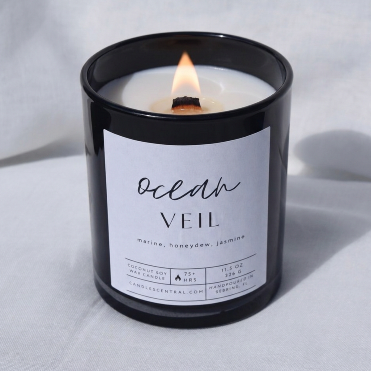 Picture of a candle burning with a label that says "Ocean Veil" along with the fragrance notes of marine, honeydew, and jasmine