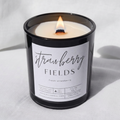 Picture of a candle burning with a label that says "Strawberry Fields" along with the fragrance note of fresh strawberry.