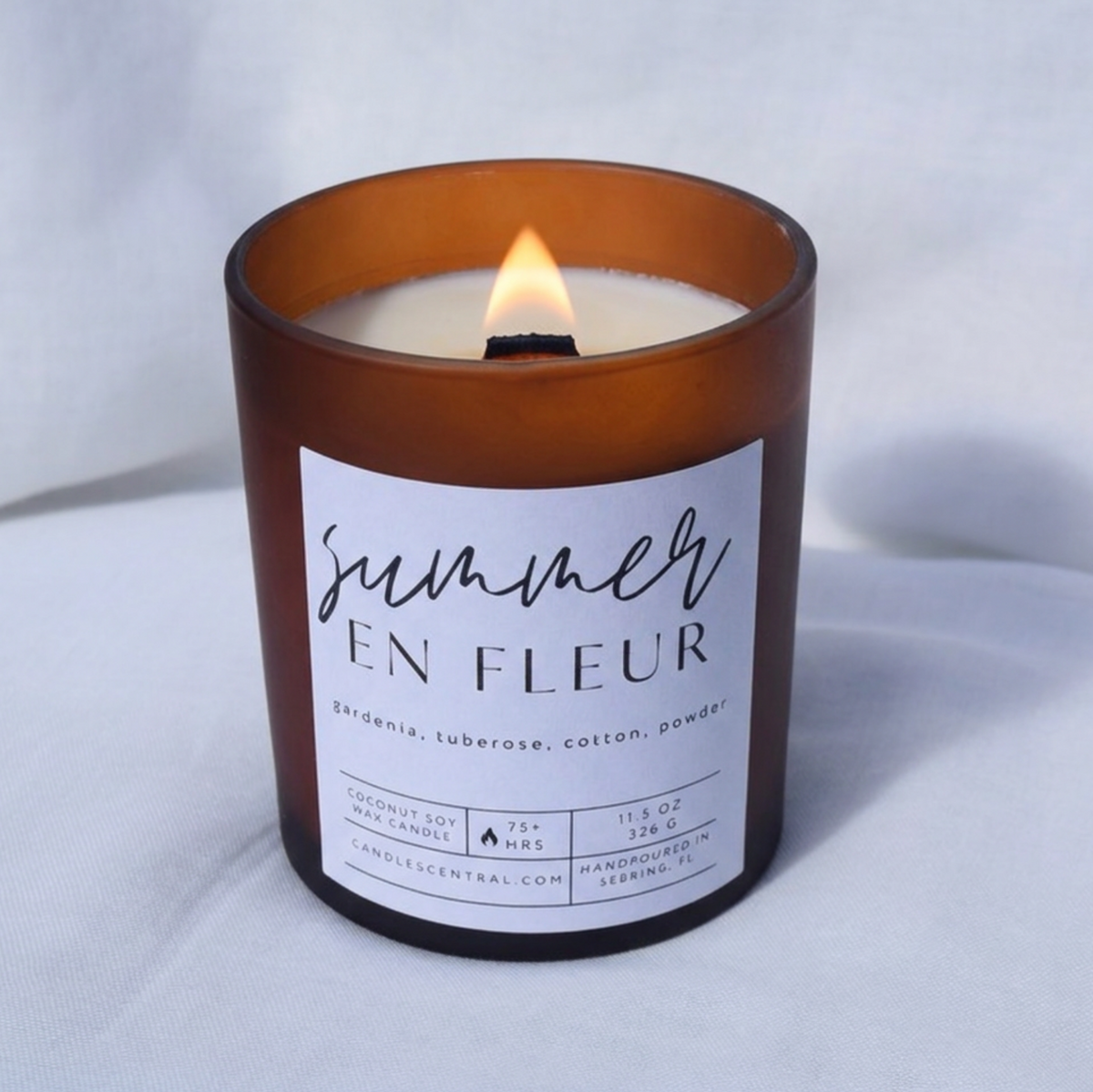 Picture of a candle burning with a label that says "Summer en Fleur" along with the fragrance notes of gardenia, tuberose, cotton, and powder