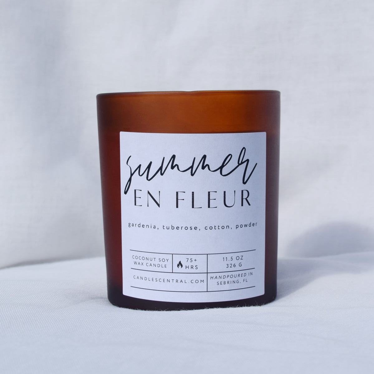 Picture of a candle with a label that says "Summer en Fleur" along with the fragrance notes of gardenia, tuberose, cotton, and powder