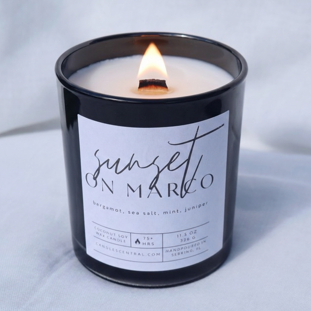 Picture of a candle burning with a label that says "Sunset on Marco" along with the fragrance notes of bergamot, sea salt, mint, and juniper