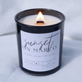 Picture of a candle burning with a label that says "Sunset on Marco" along with the fragrance notes of bergamot, sea salt, mint, and juniper