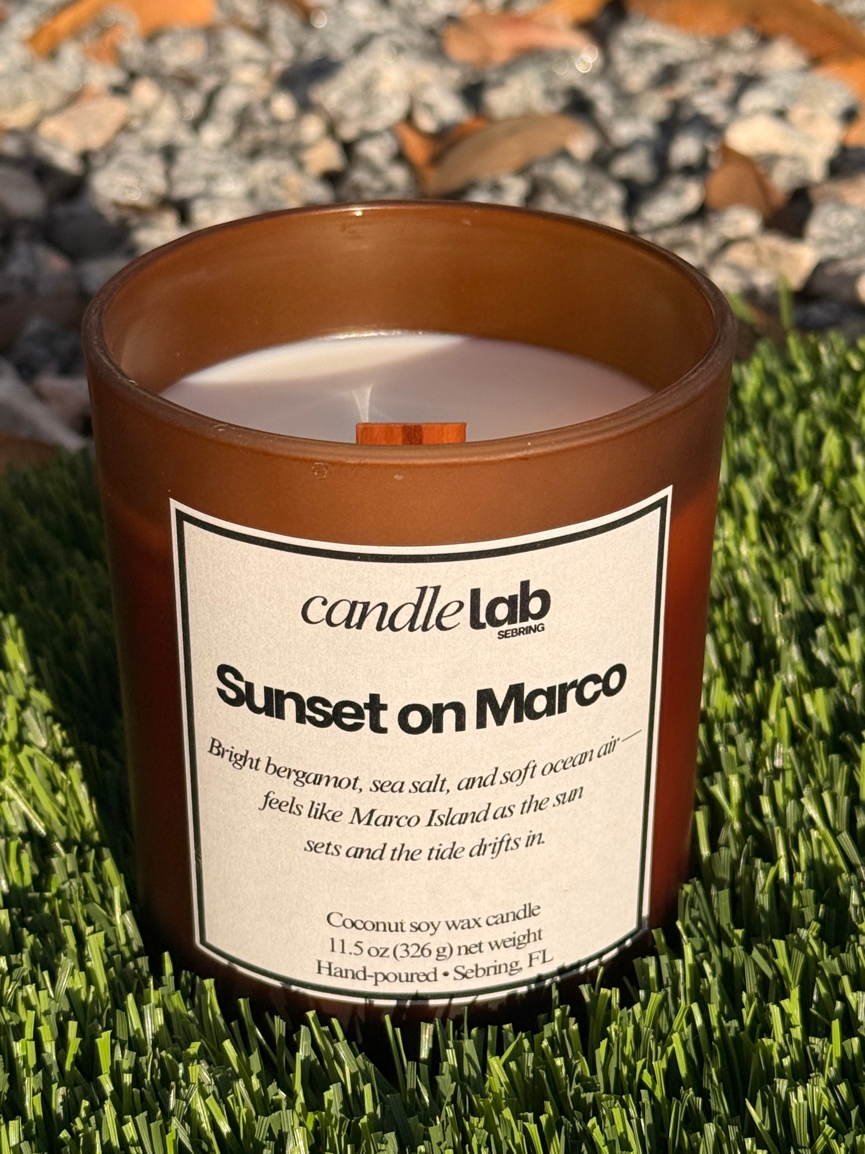 An amber glass candle with a label that says "Sunset on Marco" along with a short blurb reading "Bright bergamot, sea salt, and soft ocean air-- feels like Marco Island as the Sun sets and the tide drifts in."