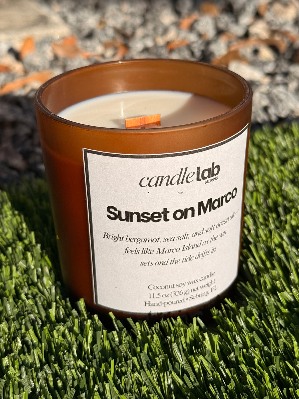 An amber glass candle with a label that says "Sunset on Marco" along with a short blurb reading "Bright bergamot, sea salt, and soft ocean air-- feels like Marco Island as the Sun sets and the tide drifts in."