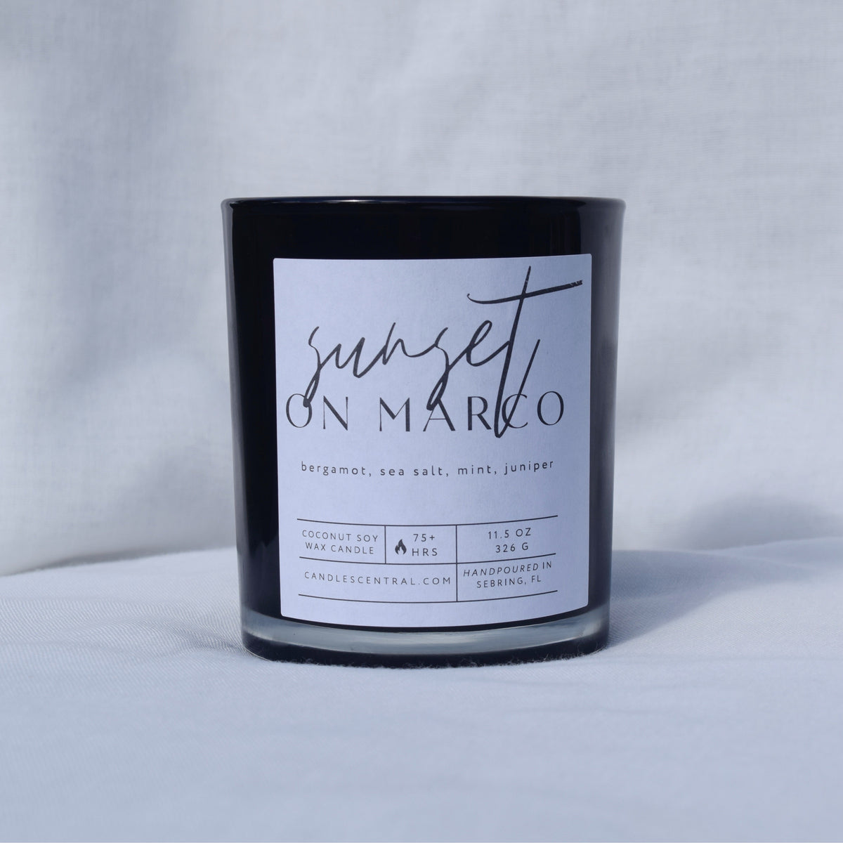 Picture of a candle with a label that says "Sunset on Marco" along with the fragrance notes of bergamot, sea salt, mint, and juniper