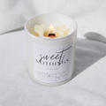 Picture of a candle burning with a label that says "Sweet Nothings" along with the fragrance notes of vanilla and sugar