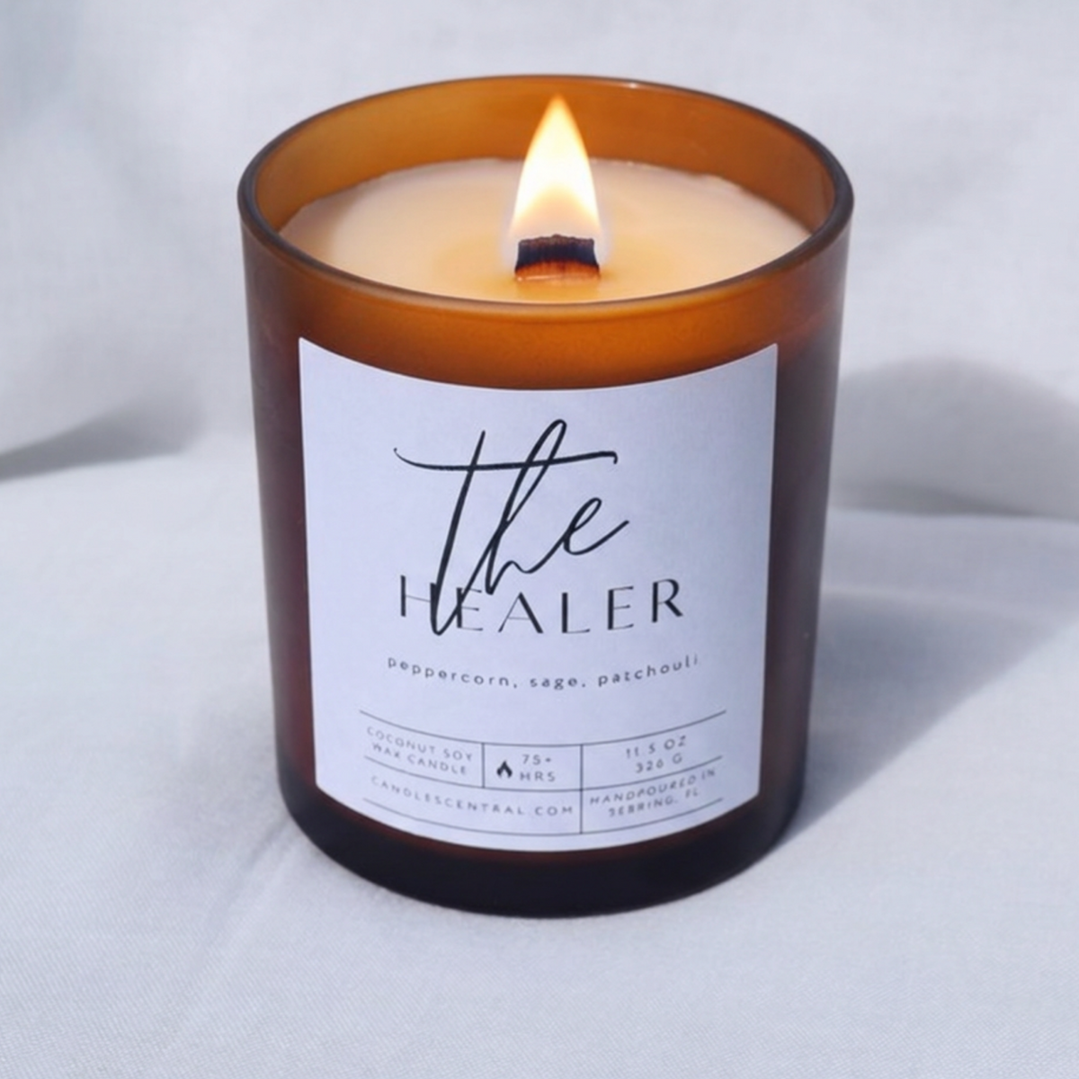 Picture of a candle burning with a label that says "The Healer" along with the fragrance notes of peppercorn, sage, and patchouli