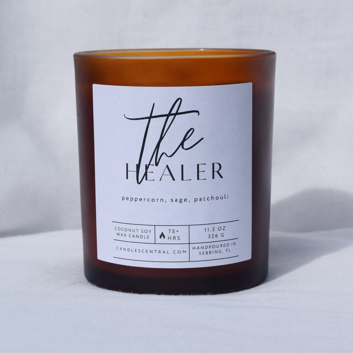 Picture of a candle with a label that says "The Healer" along with the fragrance notes of peppercorn, sage, and patchouli