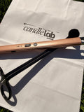 A picture of a bronze electric lighter and black wick trimmer sitting on a white bag with the words "Candle Lab Sebring" printed on the background.