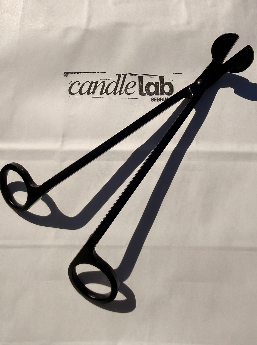 A picture of a black candle wick trimmer on a background that says "Candle Lab Sebring"