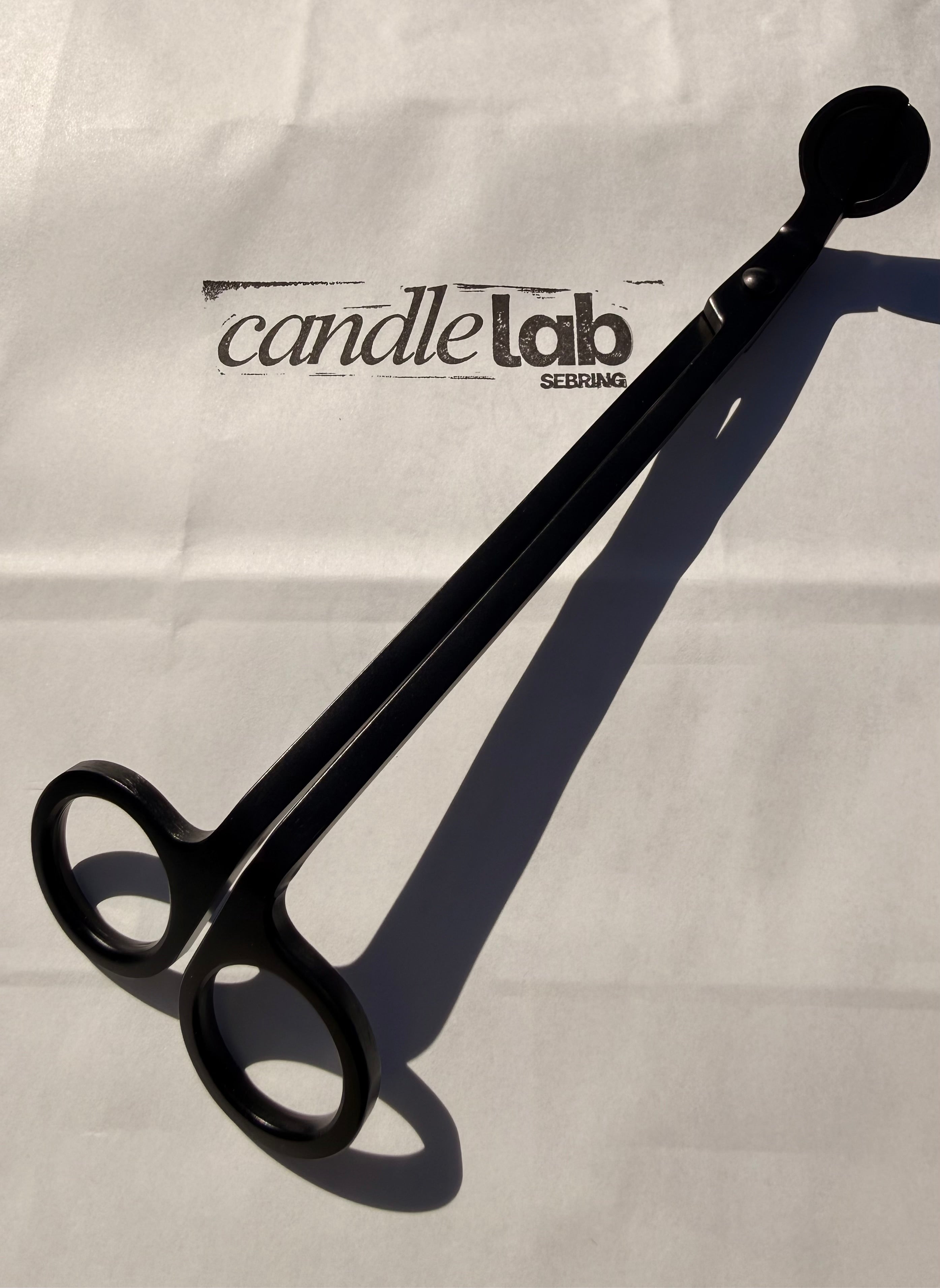 A picture of a black candle wick trimmer on a background that says "Candle Lab Sebring"